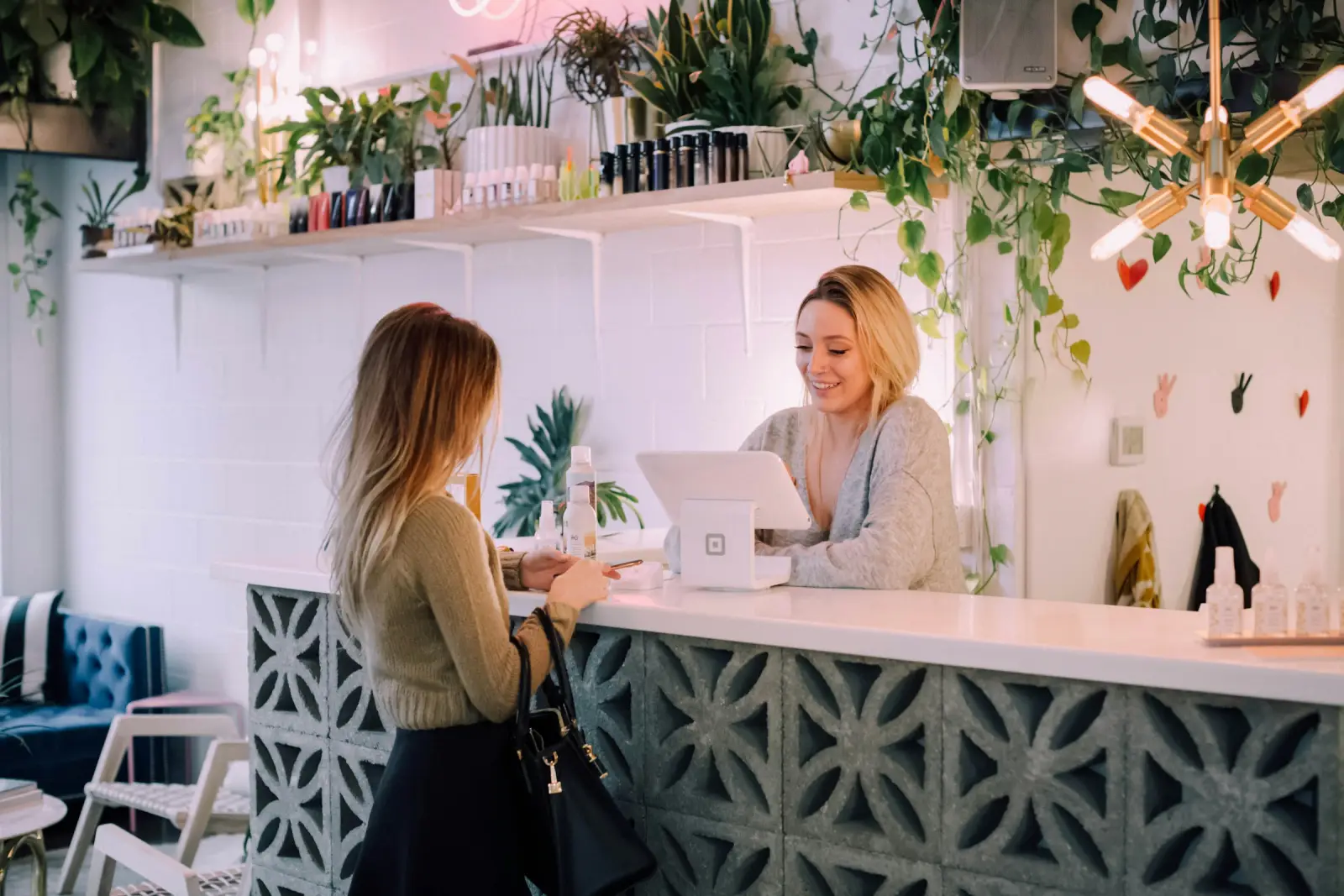 A customer at the counter of a small shop full of plants, served by a smiling owner