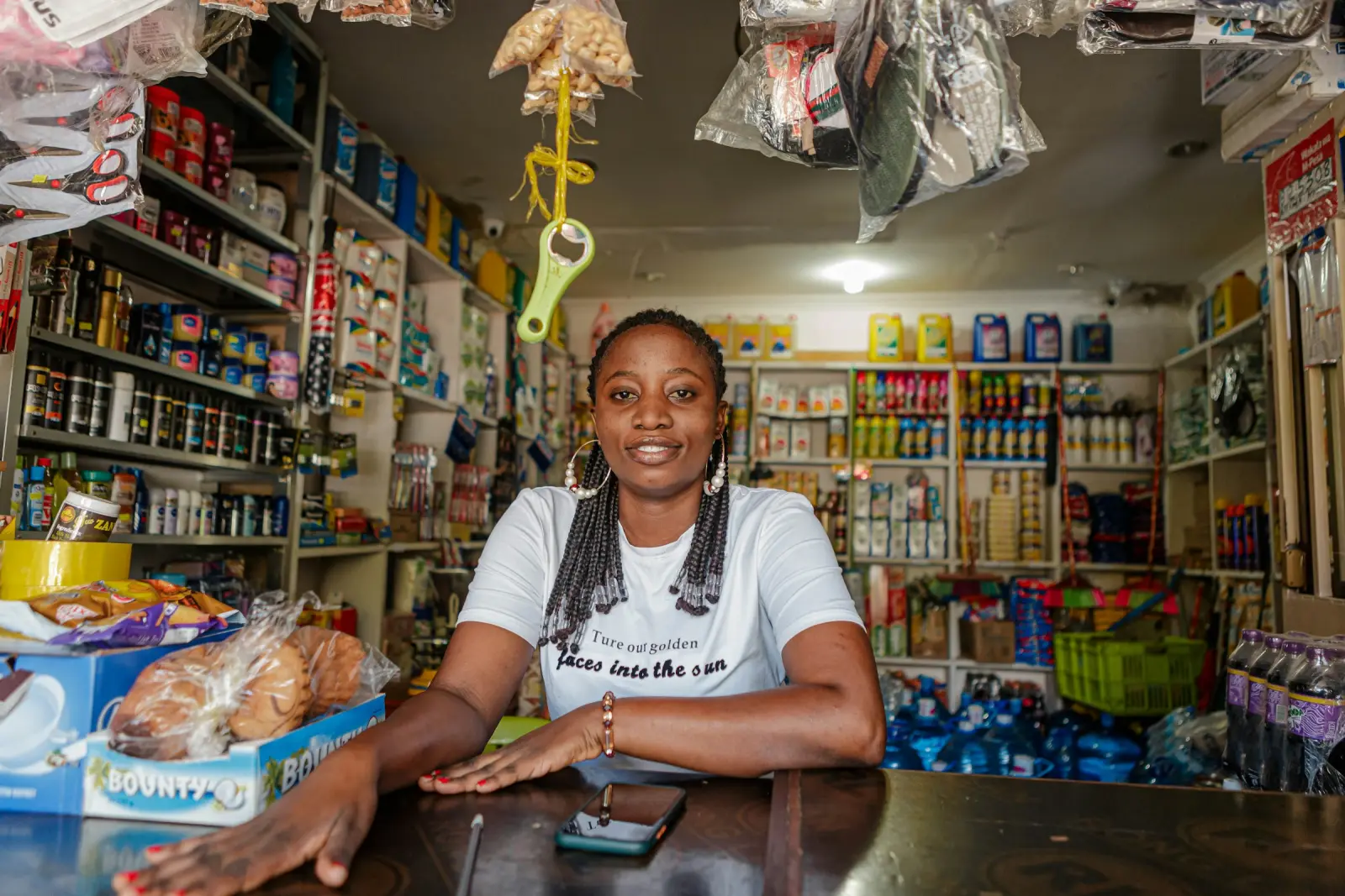 A shop owner smiling behind the counter of her small, well-stocked store